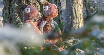Kaksi kameleonttimaskottia nojaa männynrunkoon.