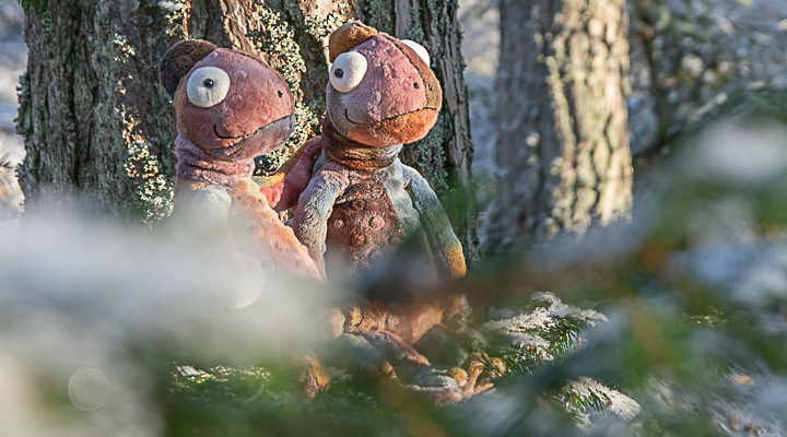 Kaksi kameleonttimaskottia nojaa männynrunkoon.